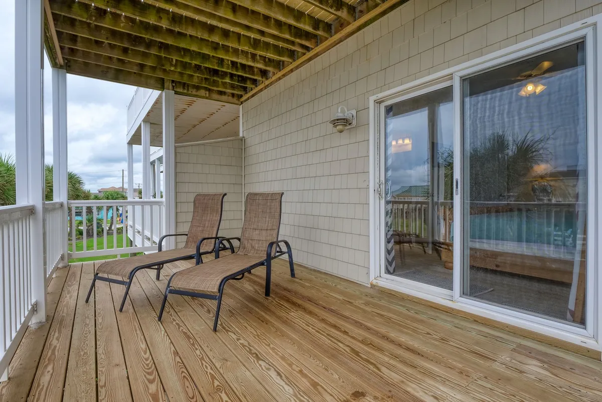 A serene exterior deck space featuring two lounge chairs and a wooden deck accessed via sliding glass doors. The deck invites guests to enjoy sunset cocktails or morning coffee, with a peaceful atmosphere and subtle hints of ocean views beyond.