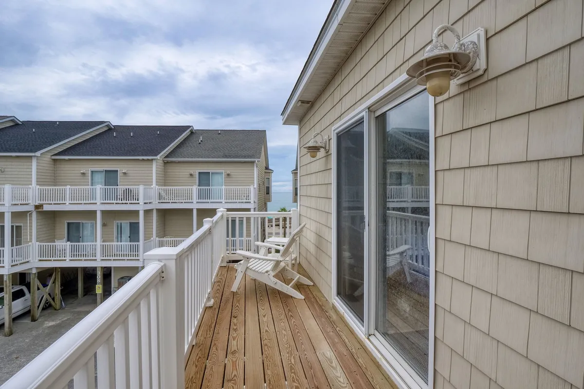 This image features a wooden deck furnished with outdoor chairs, set against adjoining buildings. The tranquil scene suggests an inviting spot for morning coffee or evening relaxation, with open air and a sense of connection to the outdoors.