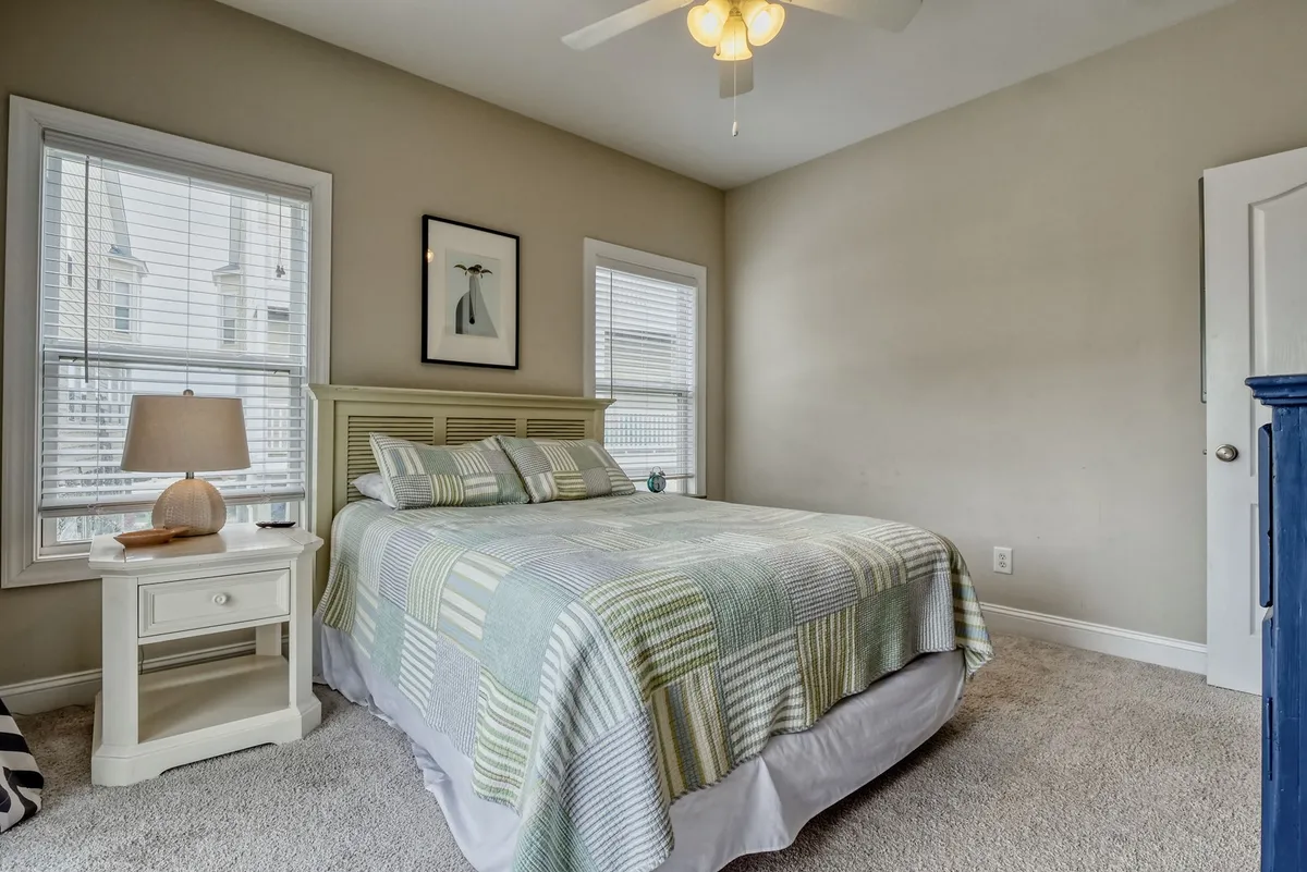 A peaceful bedroom with a plush bed, nightstand, lamp, decorative artwork, and large windows that allow for plenty of natural light. The decor is soft and serene, ideal for restful nights and rejuvenating mornings.