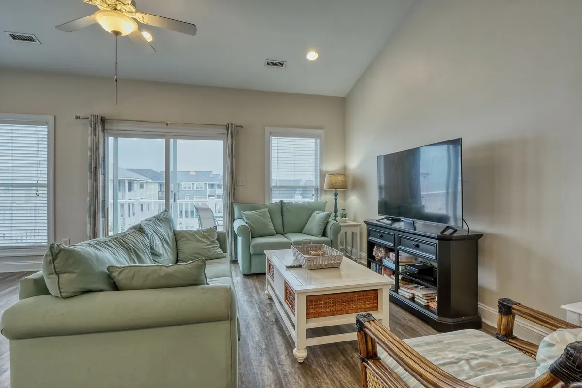 The inviting living area with a cozy sofa, coffee table, large television, and windows framing an attractive view. This space is filled with natural light, perfect for movie nights, board games, or relaxing afternoons with friends and family.