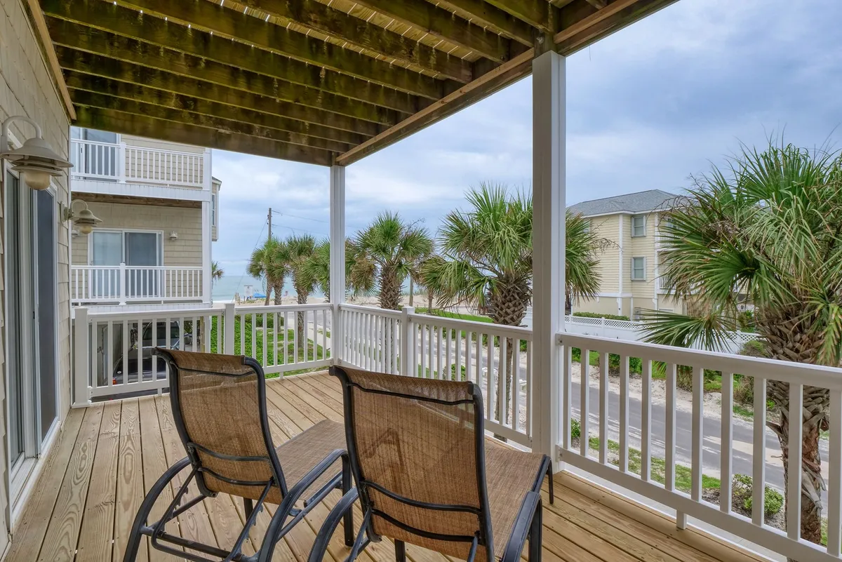 An exterior view from a deck or balcony with comfortable chairs, palm trees, and a panoramic ocean vista. The space feels calm and is ideal for soaking in sea breezes and coastal sunrises, just steps from the beach.