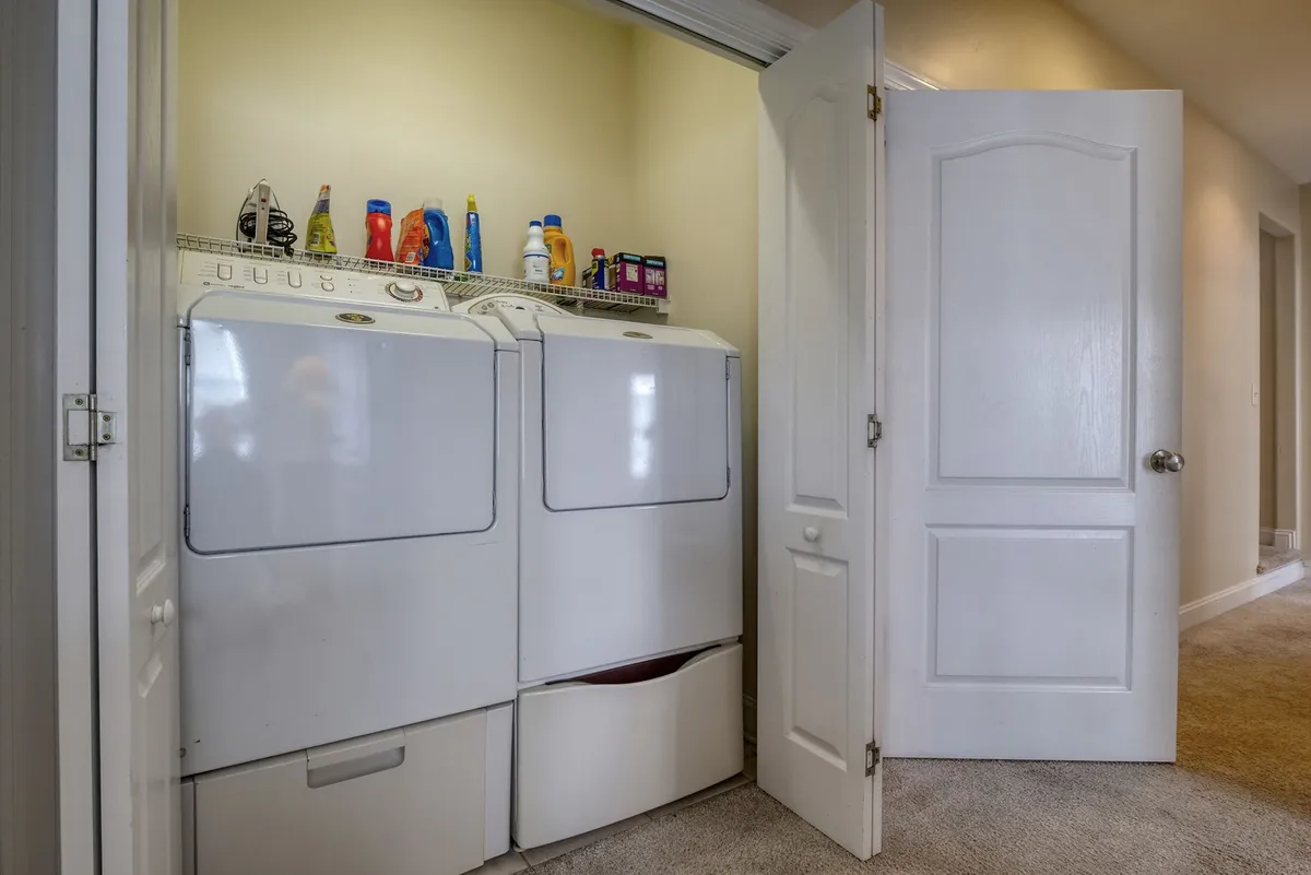 A practical laundry area with a washer, dryer, and a shelf stocked with cleaning supplies. The space is organized for efficient laundry routines, emphasizing functionality and ease for families or longer stays.