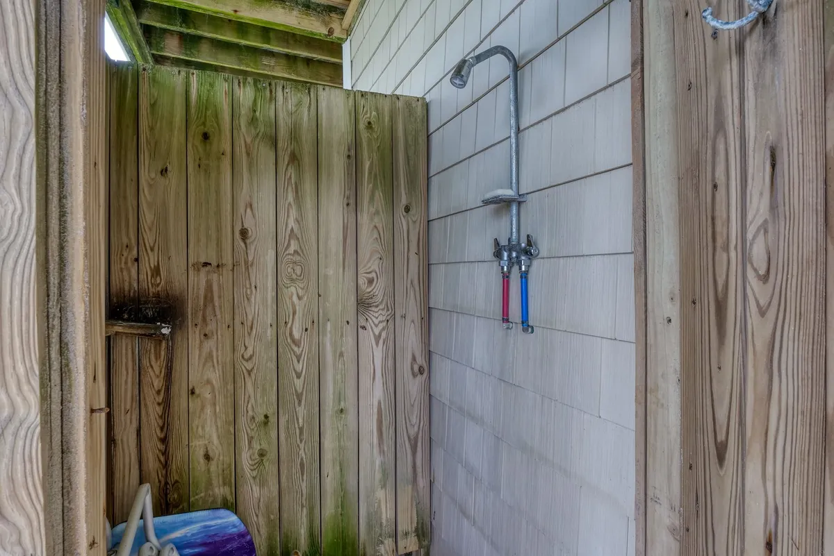 A charming enclosed outdoor shower set against wooden walls, complete with plumbing fixtures and a simple, private layout. The design evokes a fresh, beachy vibe perfect for rinsing off after visiting the shore.