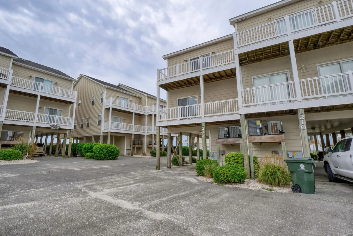 Stilted coastal buildings with spacious balconies overlook landscaped grounds. The setting hints at relaxed outdoor living, with areas for dining and family gatherings. The view suggests closeness to the ocean and vibrant local life, with space for families to gather before heading out to explore.