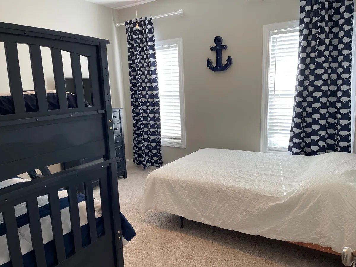 A playful bedroom featuring a bunk bed with anchor wall decor and whale-patterned curtains. The space is bright and kid-friendly, evoking a sense of adventure and togetherness perfect for families or groups.