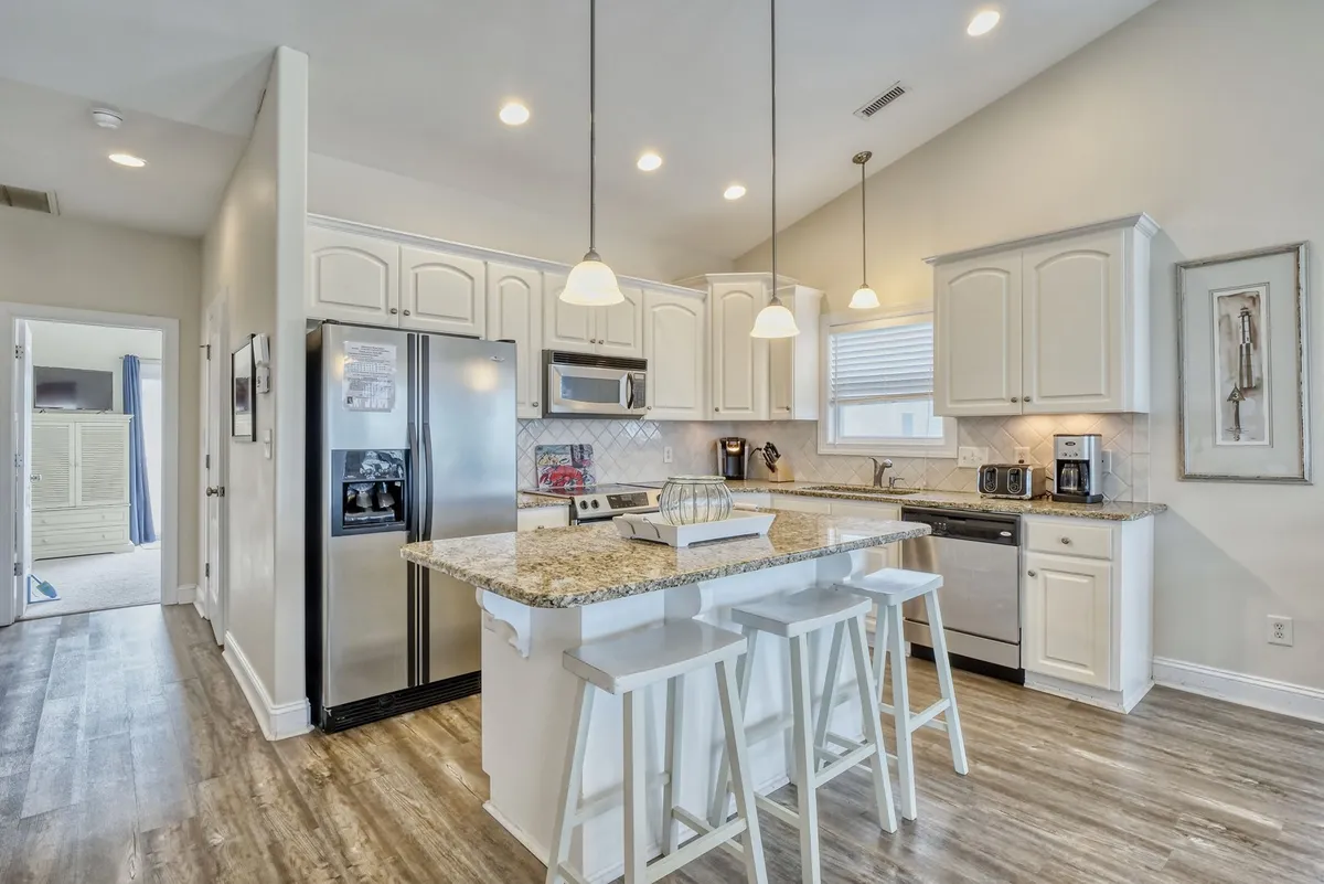 A close-up of the modern kitchen, focusing on the granite countertops, white cabinetry, stylish pendant lighting, and stainless steel appliances. The kitchen island features bar seating, suggesting a space ideal for casual meals or entertaining. The environment looks welcoming and ready for shared activities.
