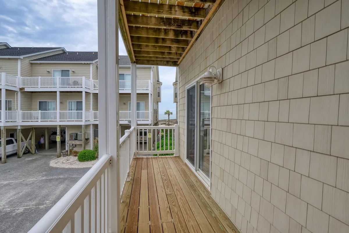 An exterior view from a wooden deck reveals surrounding coastal-style buildings and a palm tree in the distance, suggesting a relaxed community setting with fresh air and space to unwind after a swim.