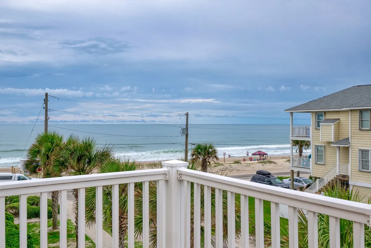 A scenic coastal view featuring ocean waves, palm trees, beach umbrellas, and nearby houses. The lively beach atmosphere hints at both family fun and relaxation, while also suggesting proximity to beach homes like Sea Star Village 212.