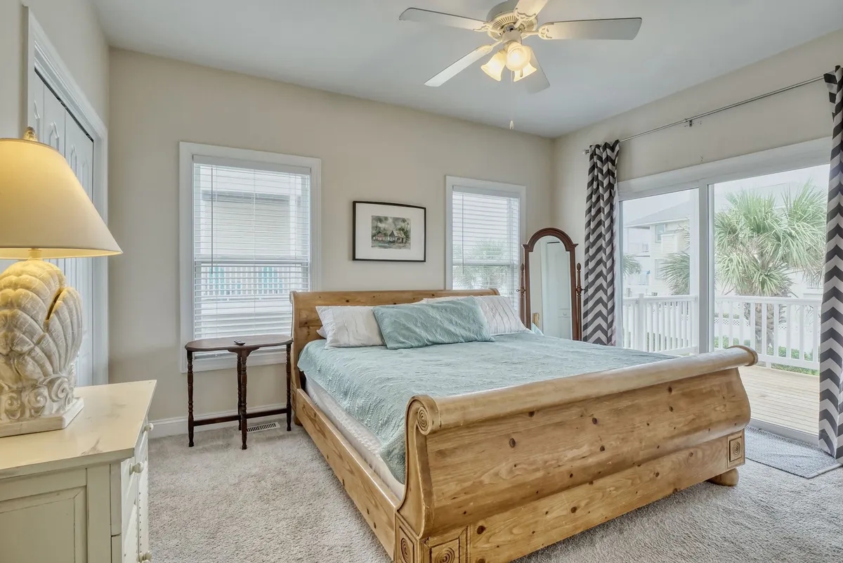 A tranquil bedroom with a wooden sleigh bed, light streaming through multiple windows with chevron curtains, and a mirrored dresser. The ambiance is calm, featuring restful decor ideal for relaxation and quiet moments.