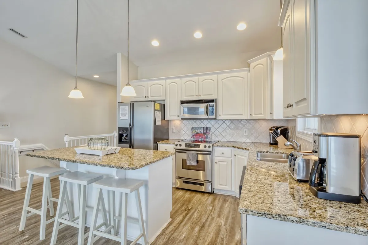 This image features a modern kitchen with a spacious granite countertop island and sleek stainless steel appliances. The layout is clearly designed for both cooking and entertaining, offering plenty of prep space and an inviting atmosphere for group activities.